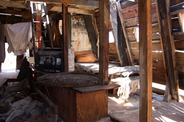 a bed in a rough wooden structure with sunlight streaming in