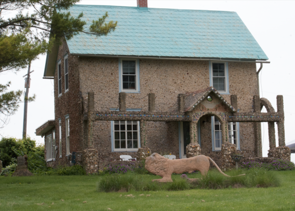 A house covered in textural concrete and rocks with a concrete lion in front of it.